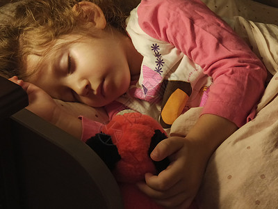 可爱的小女孩睡在床上 被一个带暖灯泡的床边桌边灯照亮背景图片
