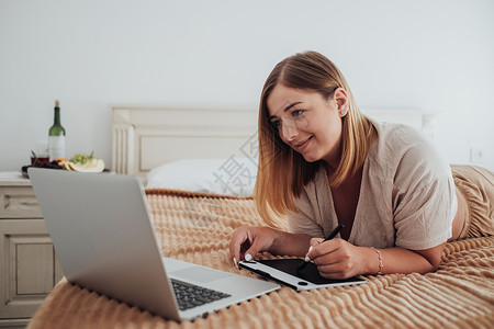 性格开朗的白人女性躺在酒店房间的床上 在数字平板电脑和笔记本电脑上工作 设计师自由职业者在工作互联网高清图片素材