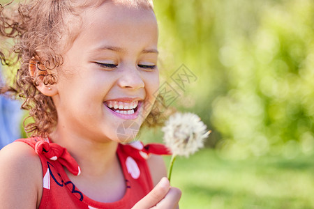 让我们看看这是否真的很神奇 一个可爱的小女孩坐在公园里拿着蒲公英的镜头图片