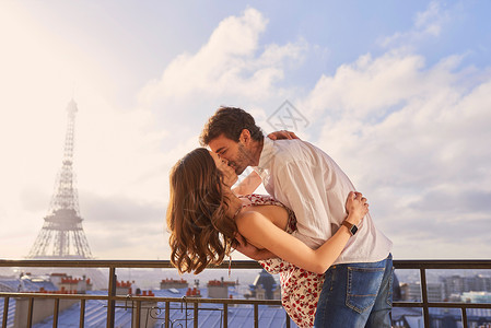 41愚你分享你不能访问巴黎而不坠入爱河 一对年轻夫妇在俯瞰法国巴黎埃菲尔铁塔的公寓阳台上分享浪漫时刻的照片背景
