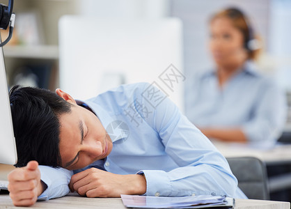 一位精疲力尽的亚洲男性呼叫中心代理人睡在办公室的办公桌前 商务人士在操作帮助台时感到过度劳累 疲倦和没有动力 懒惰的顾问通过小睡背景图片
