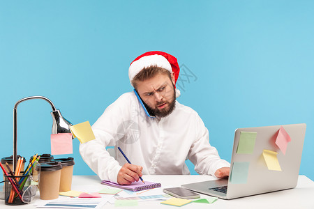 圣诞老人工作情感商务人士在蓝背景的笔记本电脑上工作蓝色男性作家桌子手机教育商务自由职业者员工帽子背景