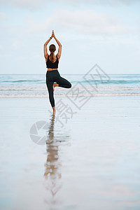树上的稳健姿势有助于你冷静思想 一个年轻女人在海滩上做瑜伽时摆出树姿势的回视镜头背景图片