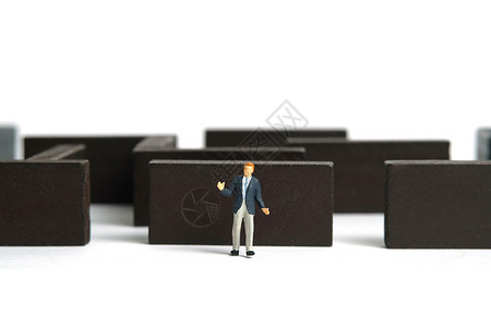 数字谜语微型人物玩具人物摄影 战略选择概念 耸耸肩的商务人士站在木制迷宫迷宫前 在白色背景上被隔离背景