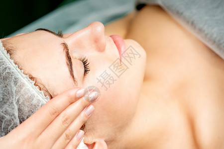 年轻女性接受面部按摩面具呵护程序美容师中心客户皱纹沙龙女士成人图片