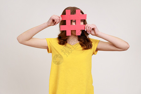 穿着黄色 T 恤 好奇的棕发年轻女性透过红色的标签标志 在社交媒体上寻找合适的帖子 从事间谍活动背景