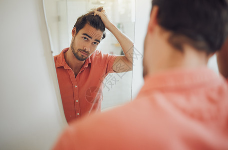 英俊的年轻白人男子抚摸着他的头发 看着浴室的镜子 男性拉他的头发 想理发 忧心忡忡的男人担心头皮屑 后退的发际线或脱发背景图片