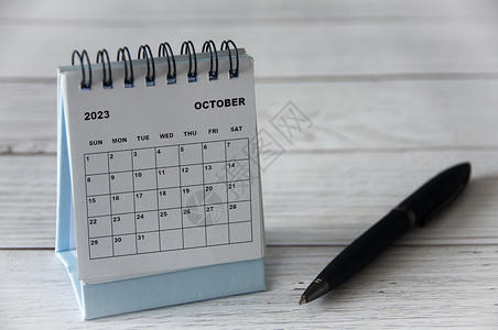 2023年10月白桌日历 木制桌子上有黑笔日程时间自由周年假期纪念日季节新年办公室空白背景图片