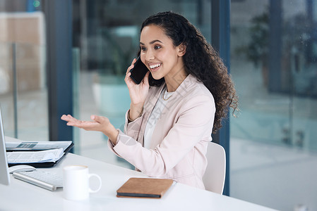 混合种族年轻快乐的混血女商务人士在办公室打电话 使用她的手机和台式电脑做手势 一位西班牙裔女商务人士坐在办公桌前微笑着 在工作中用手机聊背景
