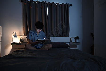 年轻人在互联网上用数码平板电脑在床上冲浪的夜拍背景图片