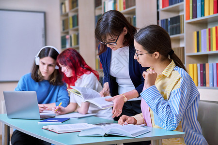 青少年学生群体和在图书馆书桌上的师范学习中学女士老师导师笔记本考试团体桌子电脑男生背景图片