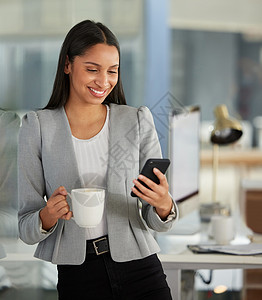 一如既往准时 一个年轻的女商务人士在现代办公室里使用智能手机喝咖啡背景