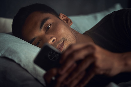 虎年更甜蜜当社交媒体比您的梦想更甜蜜时 一个年轻人躺在床上 在家里使用智能手机背景