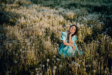 有魅力的女人坐在公园里成熟的蒲公英草坪上 穿着复古绿松石裙的女孩在乡下享受夏天 希望 快乐的概念 春天 审美肖像自由乐趣幸福微笑背景图片