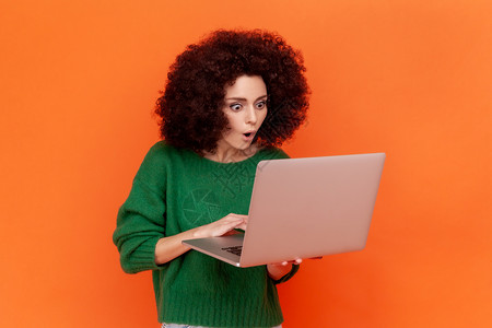编程爆炸素材身穿绿色散装毛衣的非洲发型女性在便携式电脑上工作 透过张开嘴看露台 她被震惊地描绘成一幅肖像背景