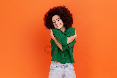 自尊自爱穿着绿色休闲毛衣 留着非洲发型的女人拥抱着自己 微笑着 感到舒适和满足 自恋的利己主义者背景