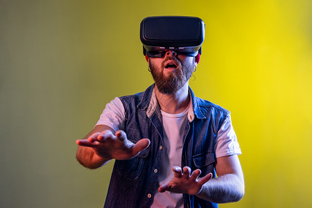 令人惊讶的人站在虚拟现实耳机上 玩电子游戏 试图触摸某些东西背景图片