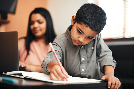 给他一些蜡笔 他就会发挥创造力 一个可爱的小男孩在家里和他的妈妈一起上色 背景是使用笔记本电脑背景图片