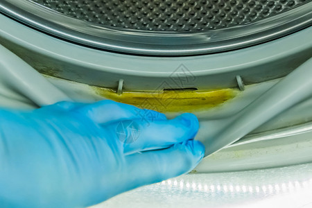 一个戴着橡胶家用手套的男人的手指向洗衣机旧滚筒压实机中的脏水残留气泡合金圆圈烘干机海豹衣服技术涂层家庭器具背景图片