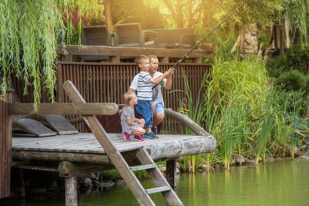 父亲和他的孩子正在一个小湖的码头上钓鱼 在宽阔的角高清图片