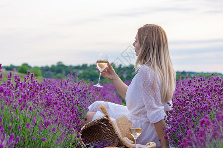 浪漫普罗旺斯一个女孩在薰衣草田的背景下拿着一杯白葡萄酒 一个女孩在薰衣草田里喝酒紫色横幅玻璃女性女士酒精场地成人农村瓶子背景
