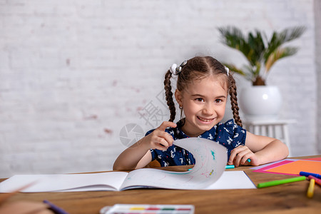 蜡笔画背景鼓动坐在桌边的小女孩 用蜡笔画画画或者在家工作绘画沉思学校铅笔童年桌子创造力快乐幼儿园艺术家背景
