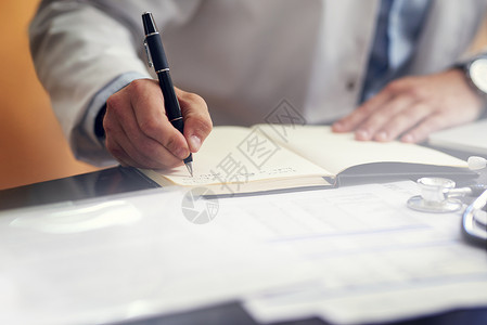 一位无法辨认的男医生 在办公室里坐在日记上写作时 他正在检查他的行程表背景