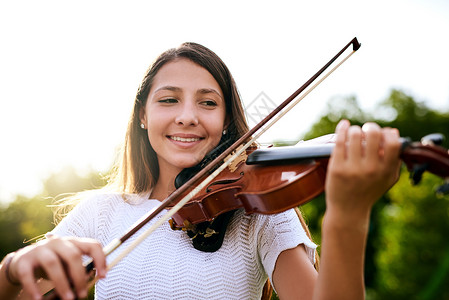 音乐振奋精神 启迪灵魂 一个快乐的年轻女孩白天站在自家后院拉小提琴背景图片