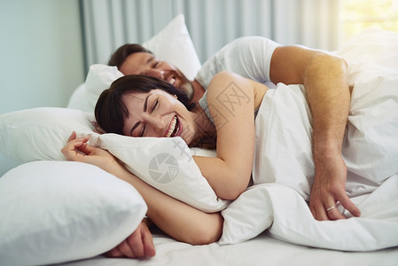 我们应该在床上多睡一会儿吗？一对放松的年轻夫妇在早上试图在床上互相拥抱睡觉背景图片