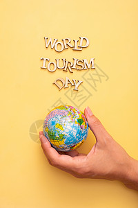 全球狂欢日世界旅游日用黄色颜色背景的木纸字母写成文字 女性掌中以全球为顶视图海报海滩铭文创造力游客地球假期旅行运输背景