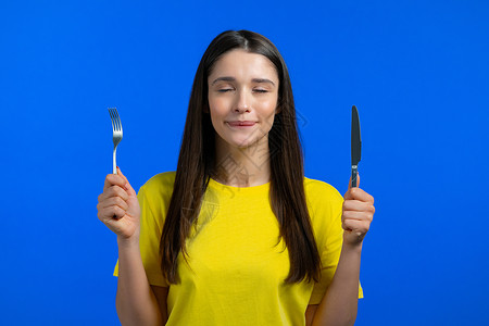 旧上的银器饥饿妇女用叉子和刀的肖像 期待着提供餐盘的女士 在蓝色工作室背景上配有餐具桌子午餐用餐营养重量厨房用具服务食物刀具背景