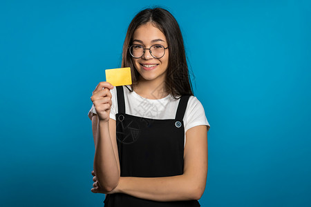 发型名片素材成功的漂亮亚洲女孩看着镜头 在蓝色工作室背景上展示无限的金信用卡微笑购物塑料成人商务女士银行业发型卡片快乐背景