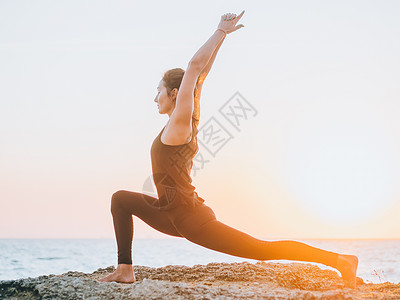 穿着黑色紧身衣裤的苗条女人在日出时在海边或海洋附近练习瑜伽 柔韧性 伸展运动 健身 健康的生活方式蓝色身体女士海滩女孩训练女性冥背景