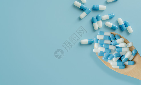 在木勺和蓝色背景上的蓝白色抗生素胶囊丸的顶部视图 抗生素耐药性 处方类药物 医疗 医药保健 抗菌药物滥用药剂处方障碍治疗药片激素背景