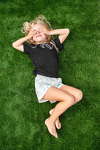 沃尔沃t6金发美女 闭着眼睛躺在绿色草地上 伸展青草 蒙上黑色T衬衫t恤孩子假期自由说谎幸福场地金发女郎童年观念背景