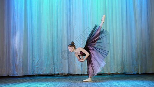 天鹅湖芭蕾舞芭蕾排练 在旧剧院大厅的舞台上 身穿淡紫色黑色连衣裙和足尖鞋的年轻芭蕾舞演员 优雅地跳着某种芭蕾舞动作 在背后抬起腿背景