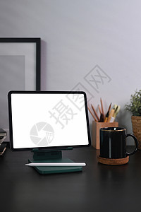 办公桌配件数字平板电脑 咖啡杯和黑木桌上的铅笔持有者背景
