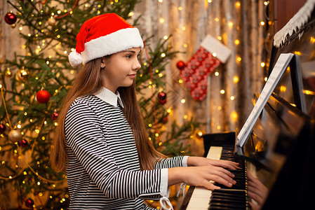 穿着红圣塔帽微笑的小女孩 在钢琴上唱着美丽的歌高清图片