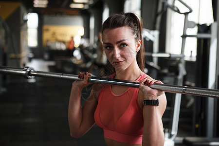 美丽的运动女子在健身房锻炼功能力量女士健美杠铃训练身体举重动机推压机背景图片