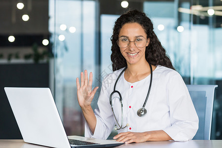 施工请注意安全一位身穿白色医用大衣的年轻专业拉丁美洲女医生的画像微笑着看着镜头举起她的手打招呼 女医生正在里面工作背景