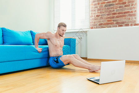 英俊的年轻运动运动员教练训练员在网上用笔记本电脑培训 在家以垫子练习运动服成人训练保健房间沙发溪流运动垫说谎肌肉背景图片