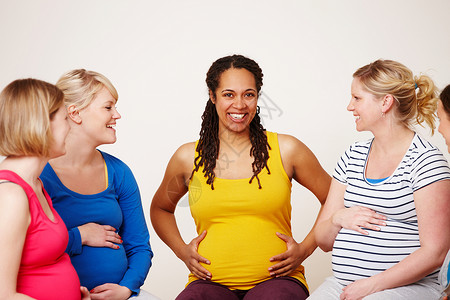 一群孕妇分享他们的经验 一群多民族的孕妇坐在一起 友好地讨论 其中一个人对着镜头微笑背景