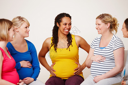 一群孕妇在整个怀孕期间互相支持 一群多民族的孕妇围成一圈微笑着背景