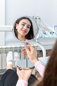 在牙科手术后照镜子的年轻女性 女青年访问治疗口腔科办公室医院牙齿内阁健康卫生镜子背景图片