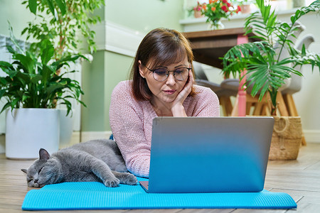 猫垫中年妇女与猫躺在运动垫上 看笔记本电脑快乐房子说谎女性宠物瑜伽平衡成人公寓互联网背景