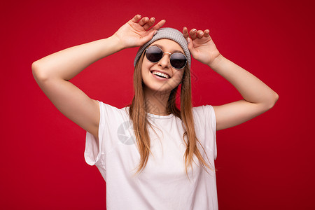 t太走秀年轻情绪积极快乐微笑滑稽笑美丽迷人的深色金发女人的肖像照片 带着真诚的情感穿着休闲的白色 T 恤 空白空间用于模拟 灰色帽子和太背景