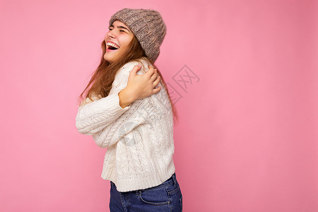 美丽积极快乐的黑发年轻女性 与色彩缤纷的背景墙隔绝 穿着休闲时尚的衣服 感觉真诚的情感 望着旁边白毛衣粉色灰帽深色帽子幸福背景图片