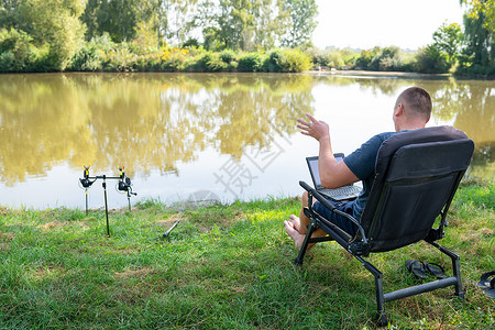 钓鱼聊天素材一名男子坐在秋湖附近的椅子上 从事笔记本电脑自由职业露营工作 机器人走出办公室 与同事通电话背景