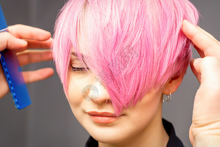 粉色发廊元用手梳发的发型师正在检查 并修补短粉红色的发型 在一个发廊里 年轻白种女人女士造型师女孩成人手指美容师刷子理发沙龙职业背景