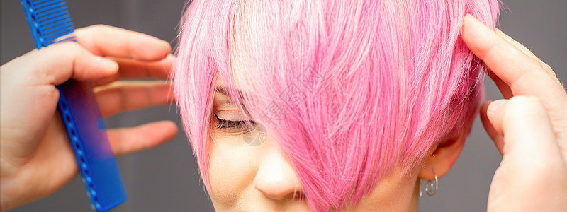 粉色发廊元用手梳发的发型师正在检查 并修补短粉红色的发型 在一个发廊里 年轻白种女人顾客店铺手臂敷料头发女孩女士客户沙龙关心背景